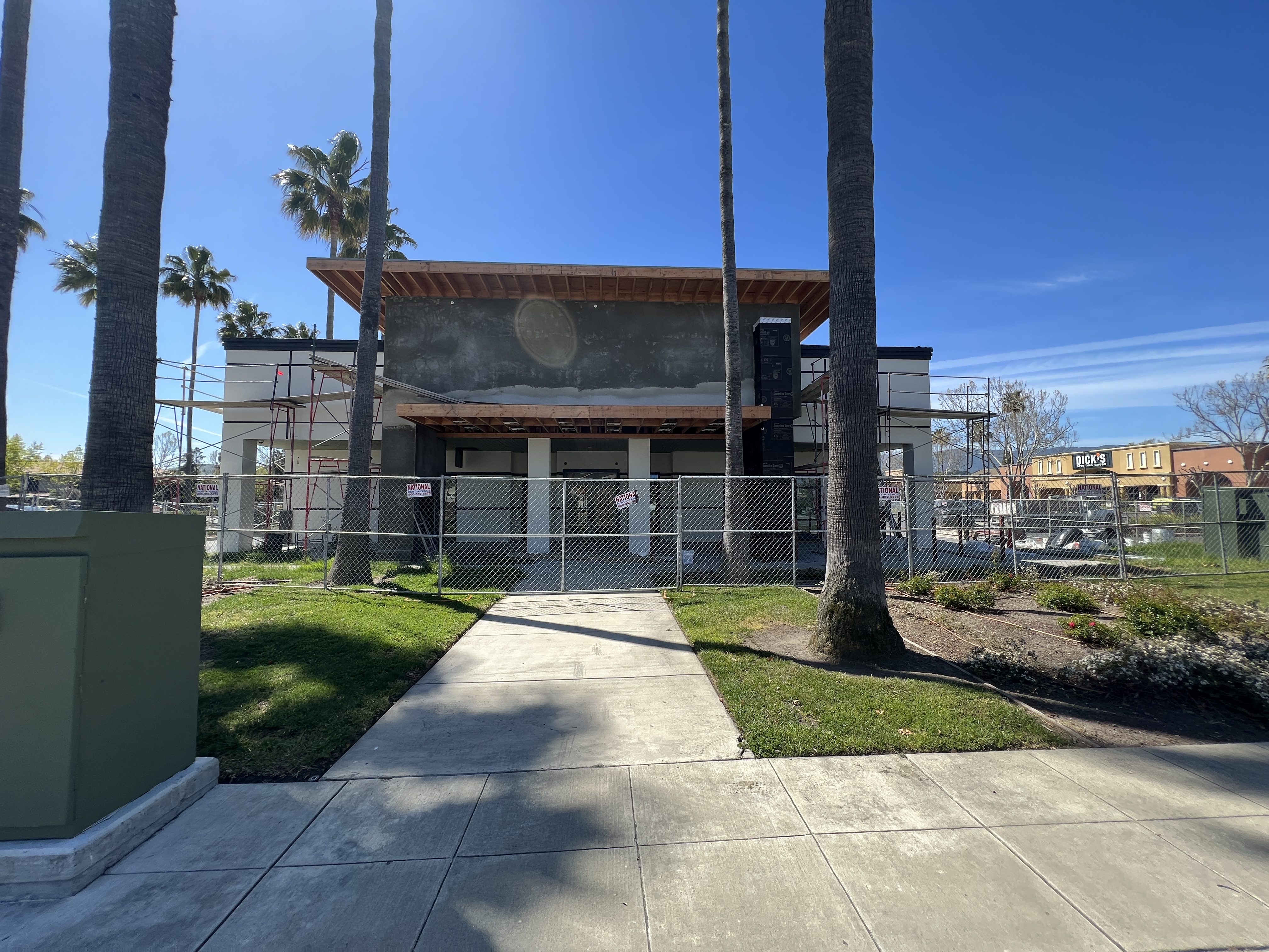 The Blossom & Bourbon building under construction in San Jose: bare stucco entry tower behind scaffolding and a chain-link fence, with no signage.