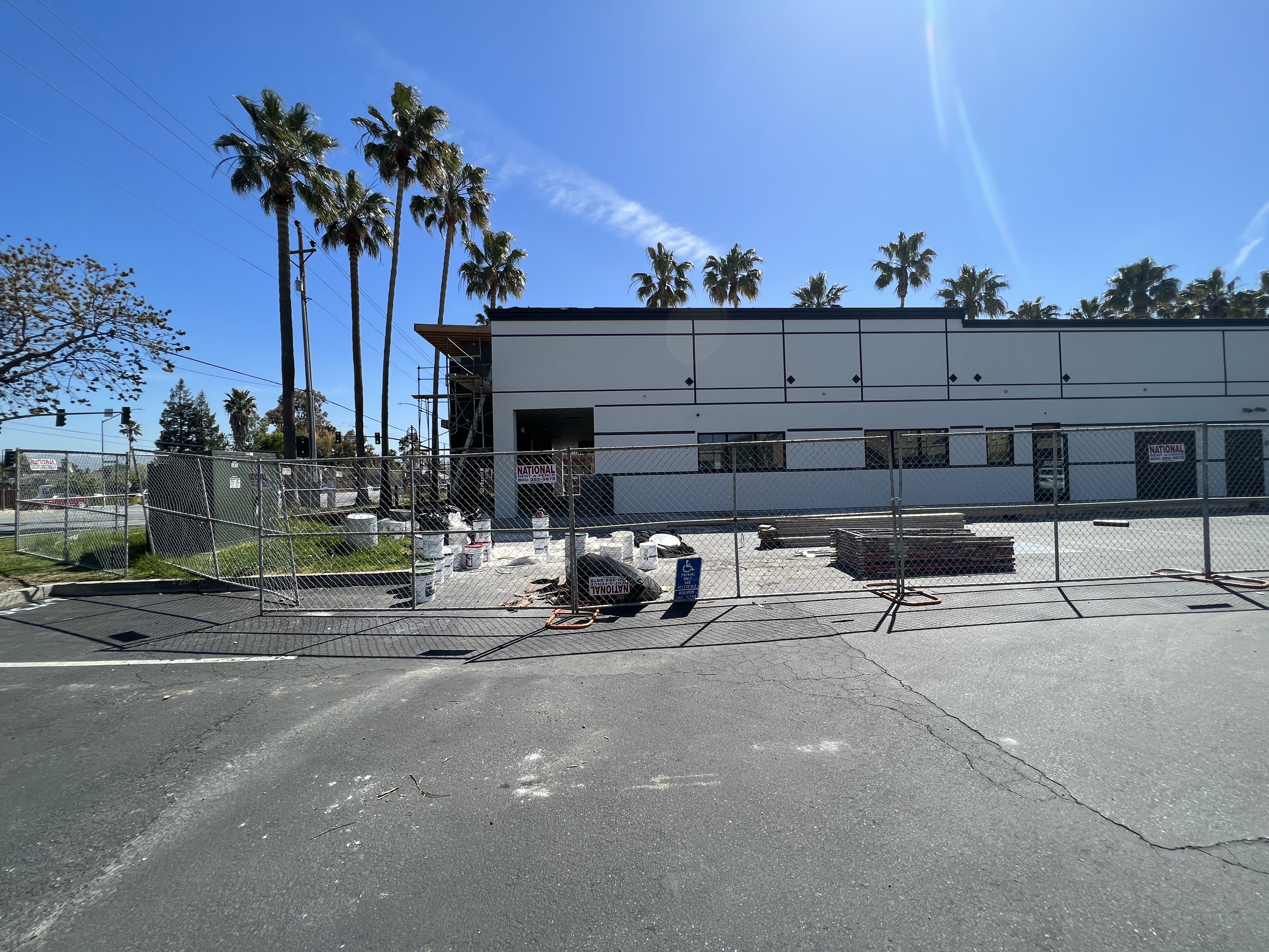 The building's white side wall before signage: a large empty stucco elevation with black trim lines and palm trees behind.