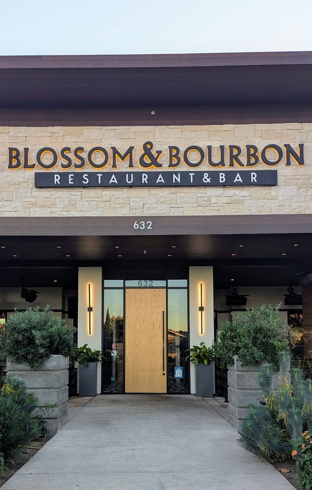 The main facade in daylight: dimensional BLOSSOM & BOURBON letters on stacked stone above the entry, halo LEDs off but the sign fully legible.