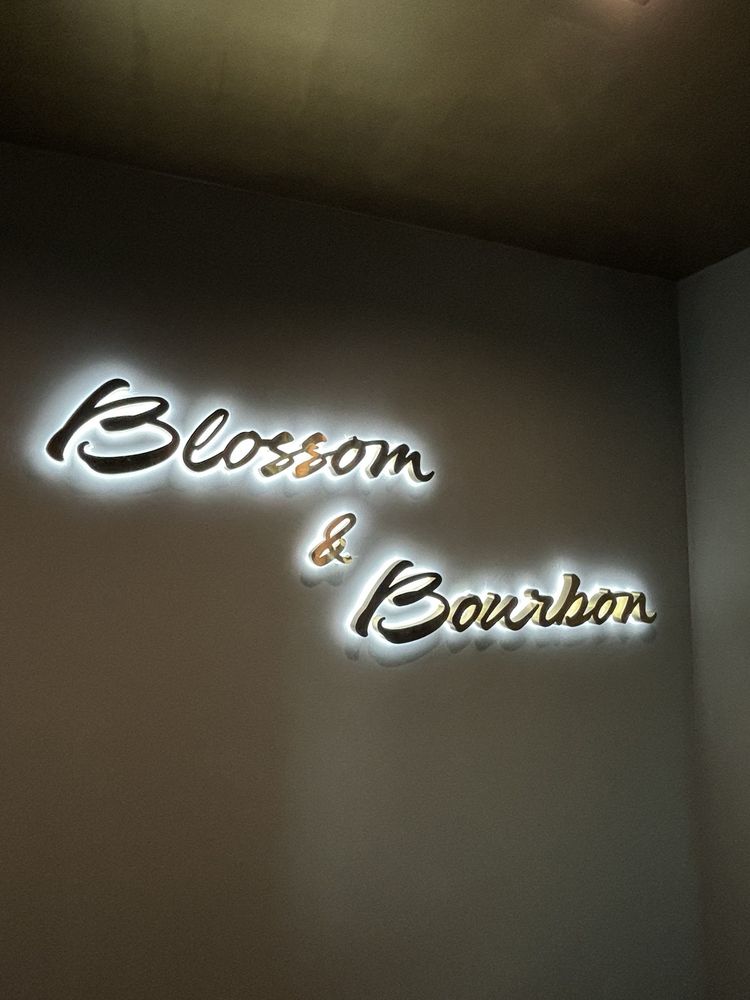 The interior script sign in low light: mirrored Blossom & Bourbon letters glowing softly against a dark wall.