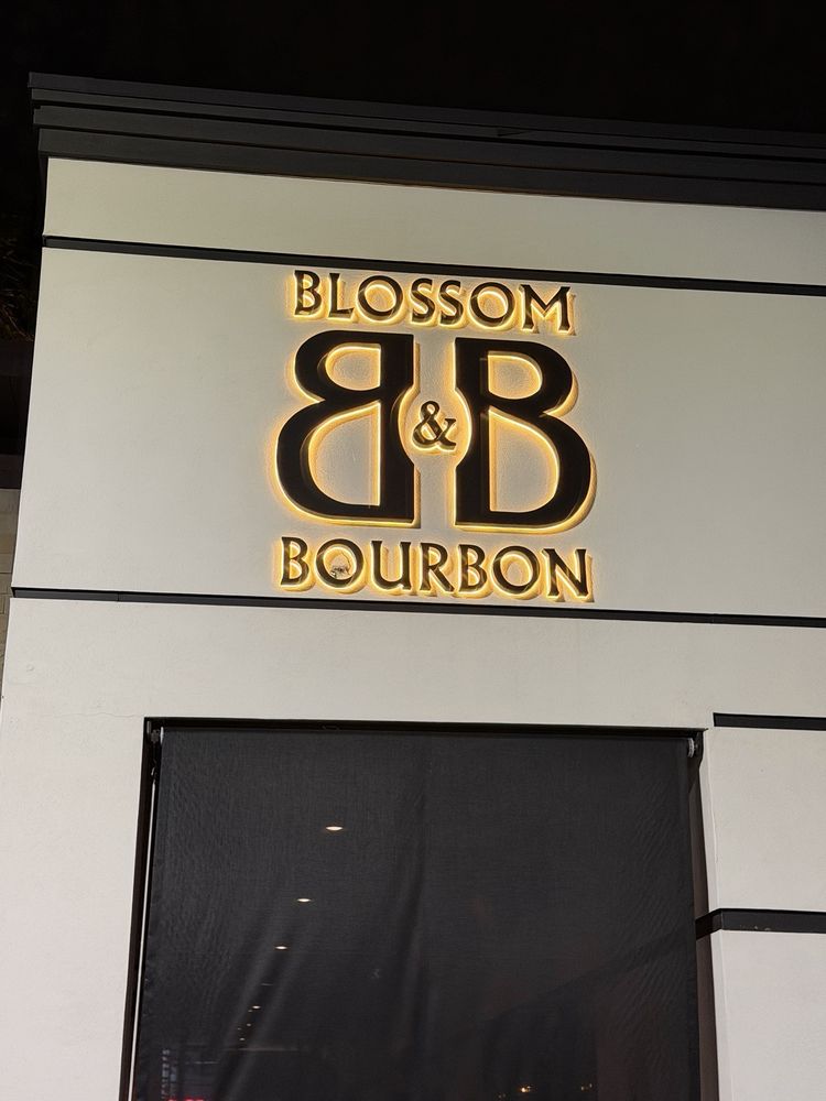 The B&B monogram at night, each letter floating in an even amber halo above the entry, the wall otherwise dark.