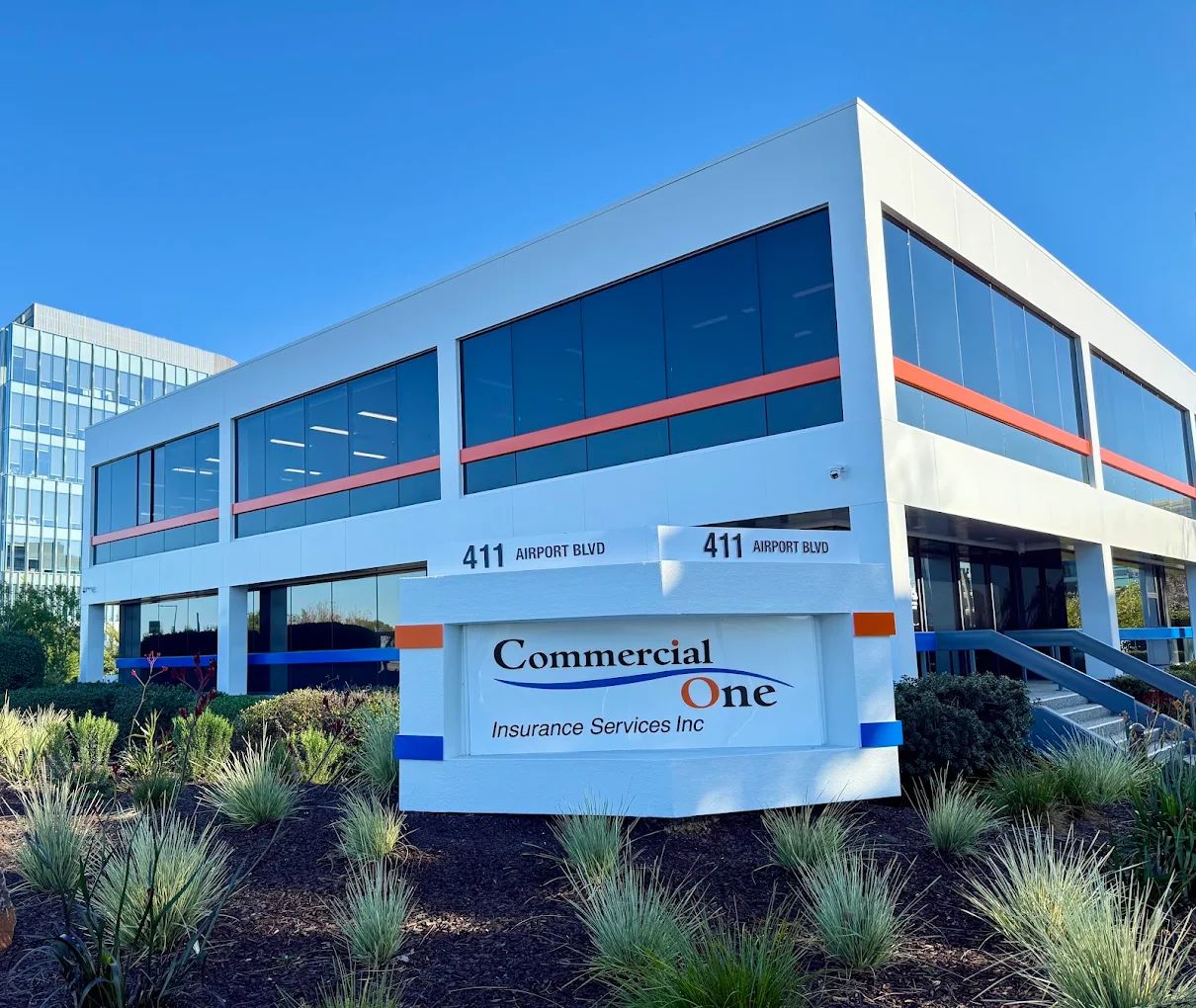 The Commercial One Insurance building at 411 Airport Blvd, Burlingame: a white two-story office building with orange stripe accents and the Commercial One monument sign in front.