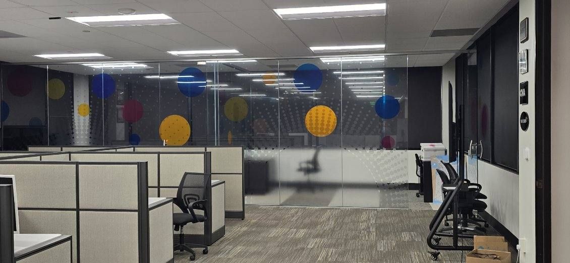 Office glass walls with a frosted privacy band and large colored dot graphics in blue, yellow, magenta, and orange, like points marked on a map.
