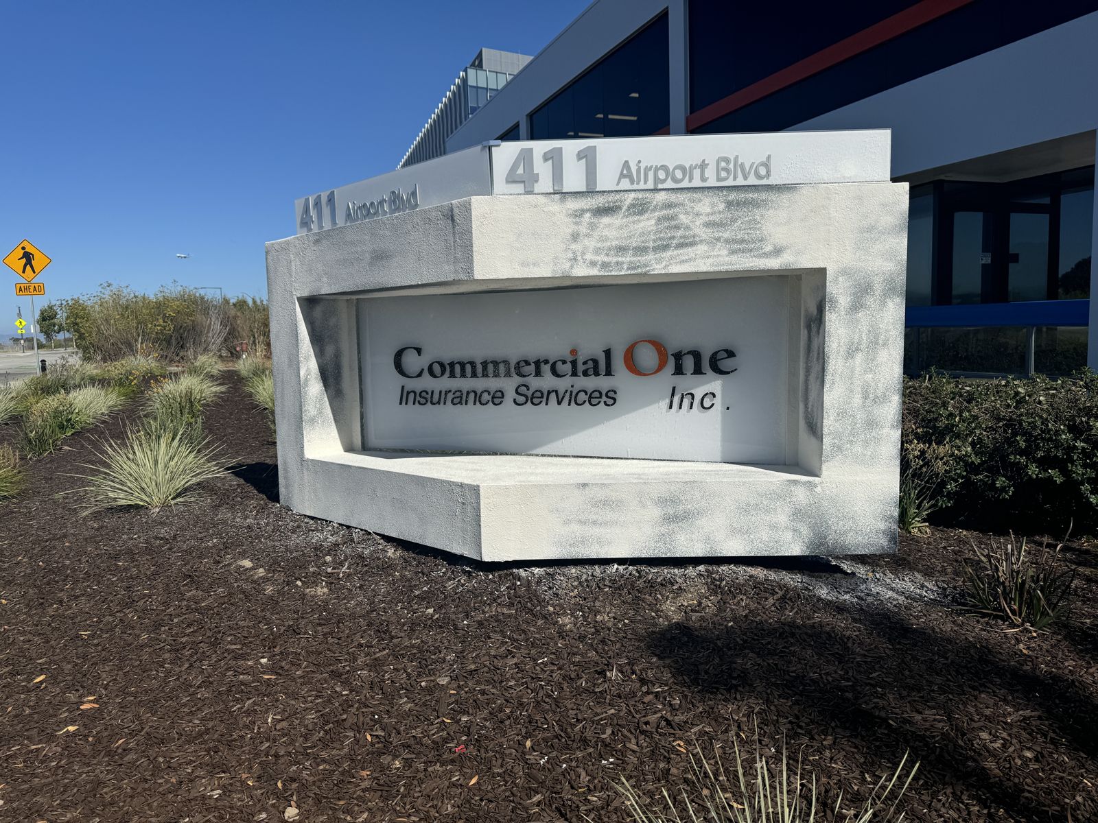 The Commercial One monument sign shaped like a ship's bow: an angled sculpted form with the company name recessed in its face and 411 Airport Blvd address letters on top.