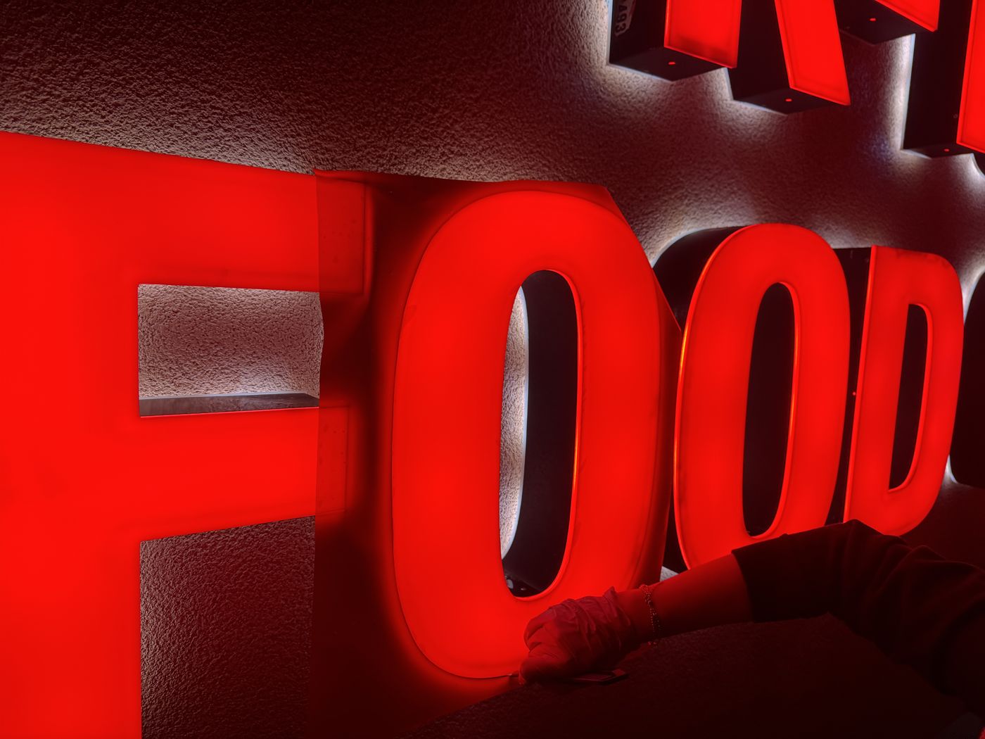 Close-up during refacing at Buena Park: a gloved hand fitting a glowing red letter face by hand, the letters lit against a stucco wall.
