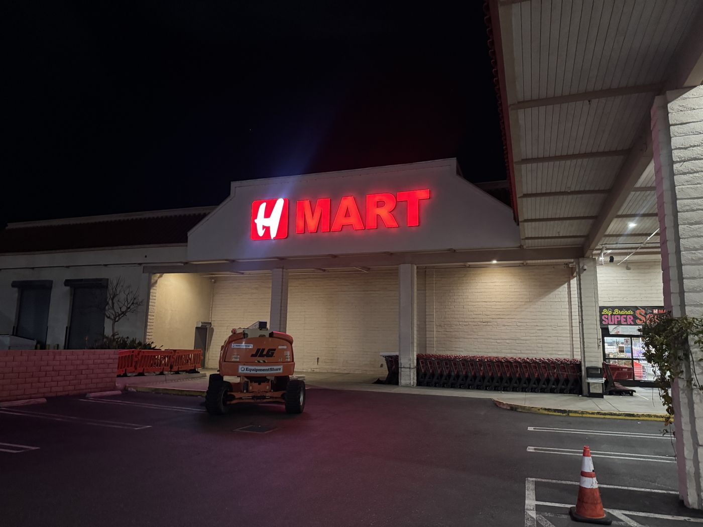 Night work at H Mart: a boom lift parked in front of the storefront while the renewed sign glows red, freshly illuminated.