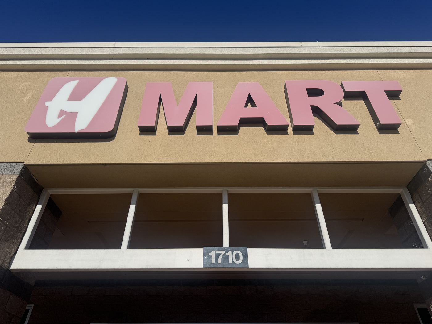 Close-up of the same H MART sign in 2025: the letters have faded from red to a soft pink.