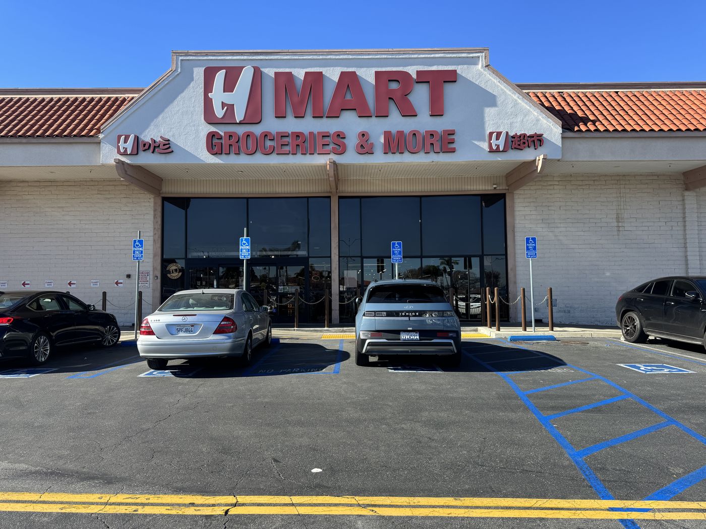 H Mart Torrance entrance before renewal, with the logo and Korean and Chinese side signs in a faded, dusty red.