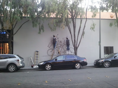 Hand-painting the bicycle wall mural on site, working from a ladder