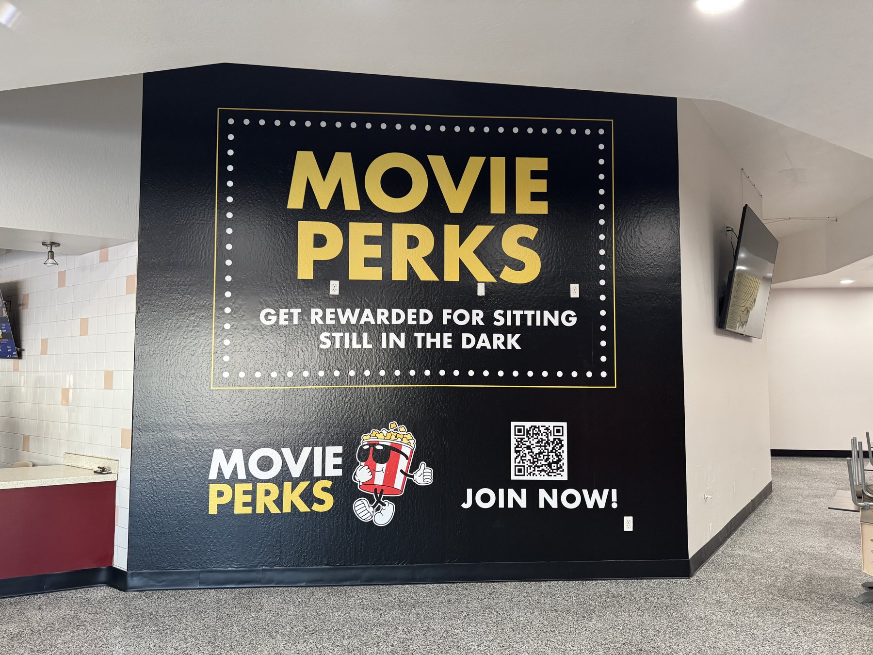 A cinema lobby wall printed as a bold Movie Perks loyalty-program advertisement with a QR code.