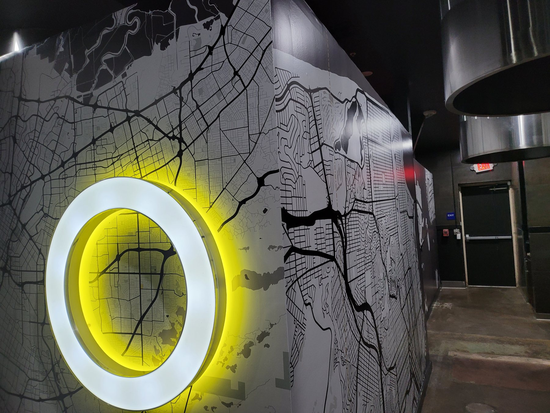 A dark map-graphic wallpaper wall with an illuminated halo-lit ring sign mounted over it — flat print gaining depth and light from the dimensional sign.