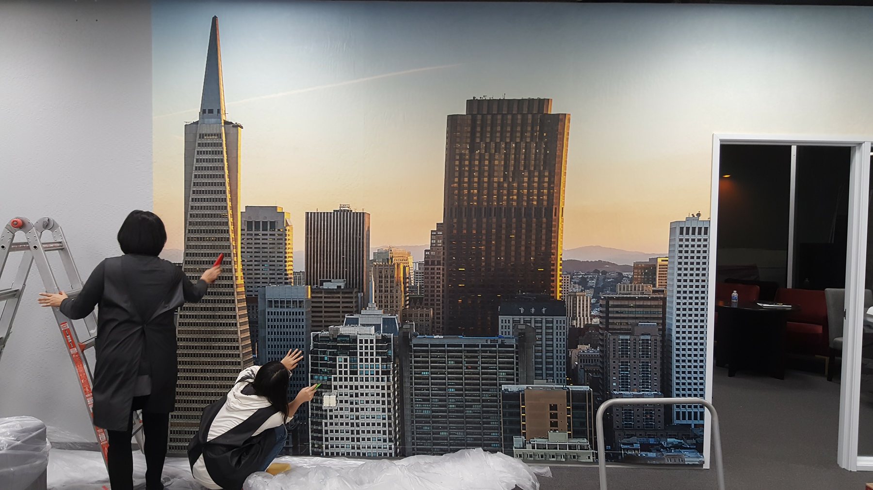 Two DT Signs installers applying a San Francisco skyline wallpaper mural across an office wall, panel by panel.